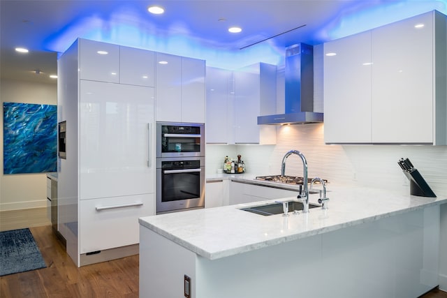 kitchen with wall chimney exhaust hood, white cabinets, and kitchen peninsula