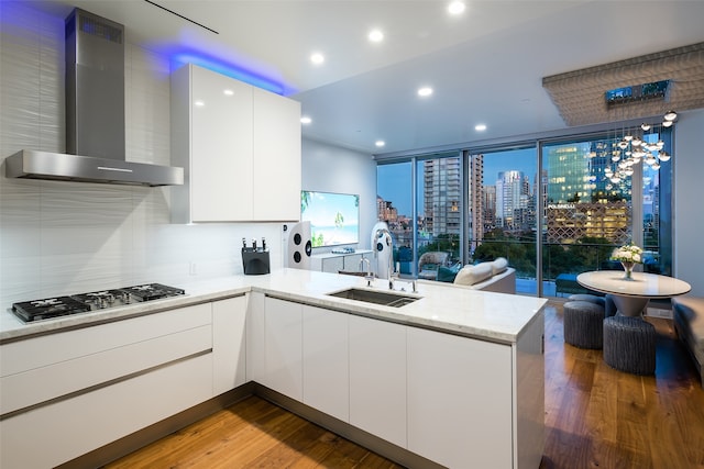 kitchen with sink, stainless steel gas stovetop, white cabinetry, wall chimney range hood, and hardwood / wood-style floors