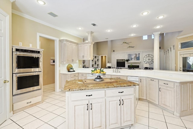 kitchen featuring appliances with stainless steel finishes, kitchen peninsula, light tile patterned floors, crown molding, and decorative columns