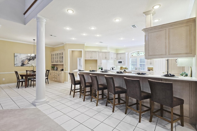 kitchen with light tile patterned flooring, a breakfast bar area, decorative columns, a notable chandelier, and crown molding