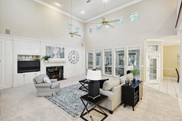 living room with ceiling fan, ornamental molding, light tile patterned floors, a high end fireplace, and a high ceiling