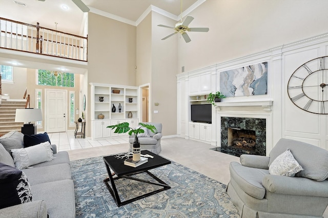 living room with ceiling fan, crown molding, light carpet, a fireplace, and a towering ceiling