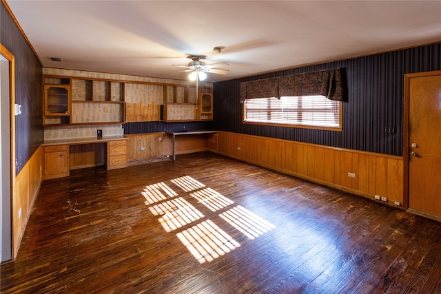 kitchen featuring dark wood-type flooring, built in desk, ceiling fan, and wooden walls