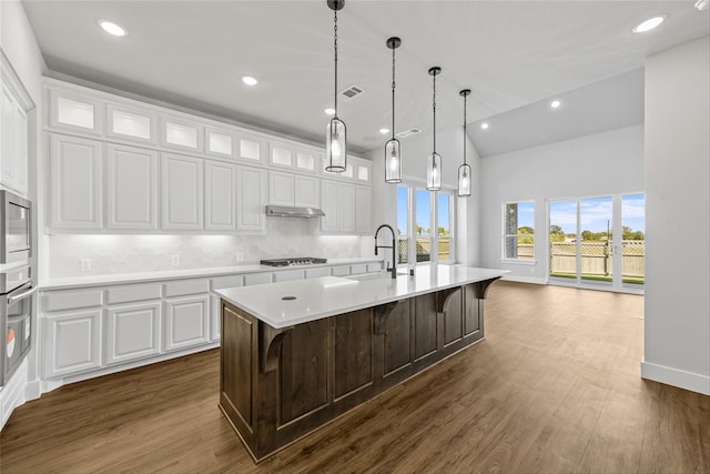 kitchen with tasteful backsplash, a breakfast bar, white cabinets, dark hardwood / wood-style floors, and an island with sink