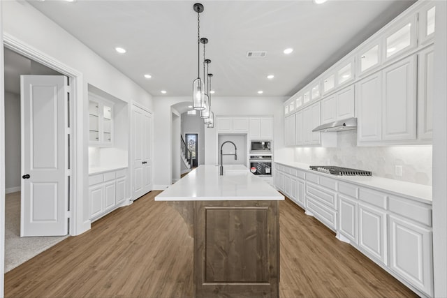 kitchen with stainless steel appliances, a kitchen island with sink, dark wood-type flooring, white cabinets, and hanging light fixtures