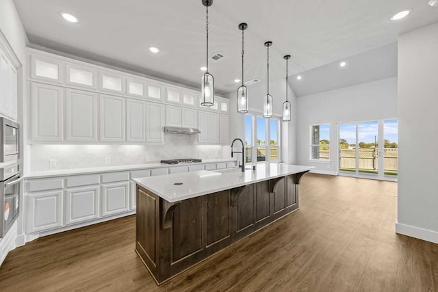 kitchen featuring a center island with sink, dark hardwood / wood-style flooring, a kitchen bar, and white cabinetry