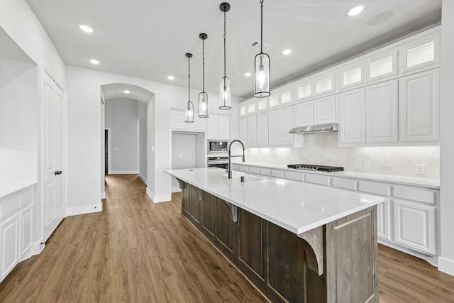 kitchen featuring sink, stainless steel appliances, dark wood-type flooring, a center island with sink, and white cabinets