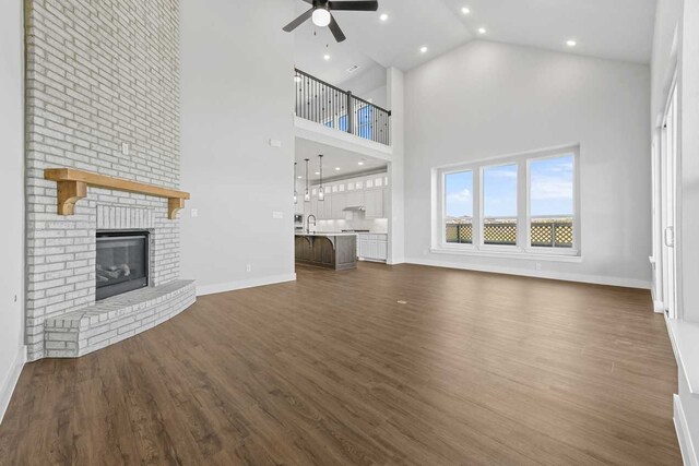 unfurnished living room featuring dark hardwood / wood-style flooring, high vaulted ceiling, and a brick fireplace