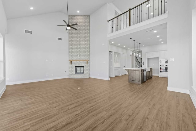 unfurnished living room featuring ceiling fan, sink, hardwood / wood-style flooring, high vaulted ceiling, and a fireplace