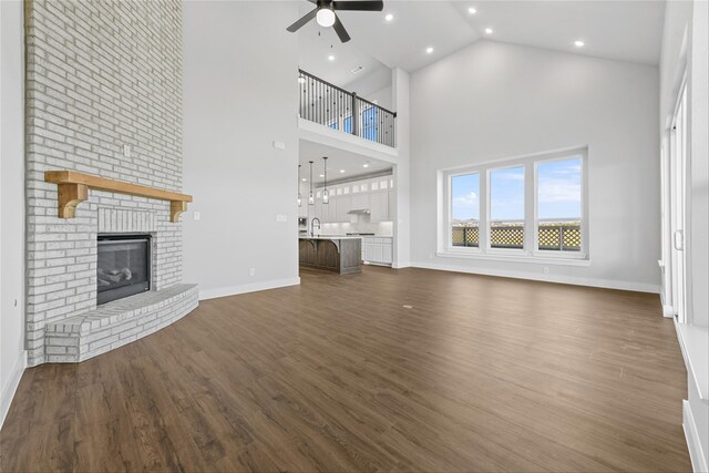 unfurnished living room featuring ceiling fan, dark wood-type flooring, high vaulted ceiling, and a brick fireplace