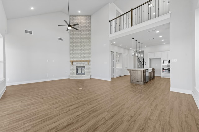 unfurnished living room featuring ceiling fan, wood-type flooring, high vaulted ceiling, and a brick fireplace