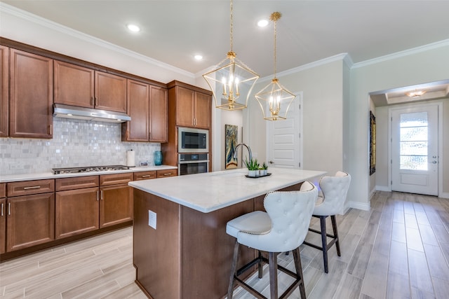 kitchen with a kitchen bar, hanging light fixtures, light hardwood / wood-style floors, stainless steel appliances, and a center island with sink