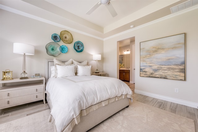 bedroom featuring ensuite bath, a tray ceiling, ceiling fan, crown molding, and light hardwood / wood-style flooring