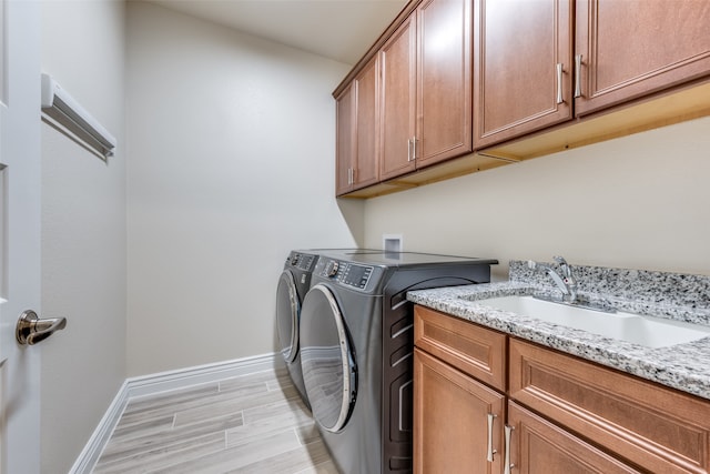 washroom with sink, cabinets, light wood-type flooring, and washing machine and clothes dryer