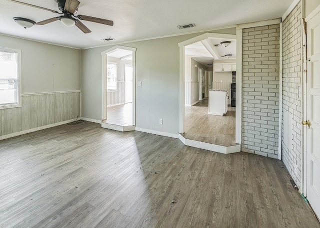 empty room with ceiling fan, hardwood / wood-style flooring, crown molding, and wood walls