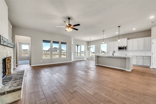 unfurnished living room with a fireplace, light hardwood / wood-style flooring, ceiling fan, and sink