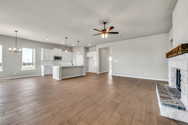 unfurnished living room featuring sink, a fireplace, ceiling fan with notable chandelier, and light wood-type flooring