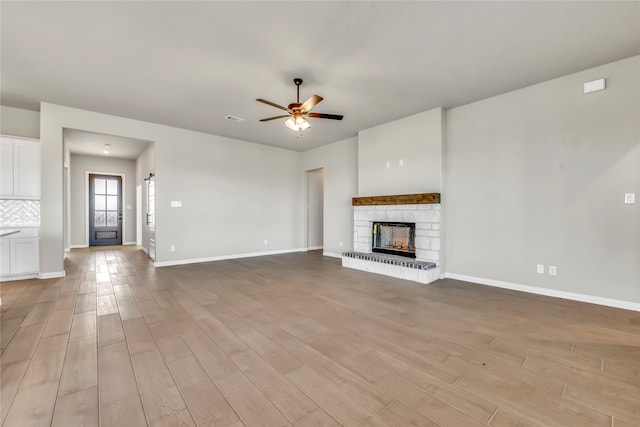 unfurnished living room with light wood-type flooring, a stone fireplace, and ceiling fan