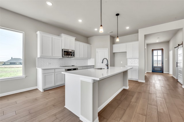 kitchen featuring a kitchen island with sink, light hardwood / wood-style flooring, white cabinets, and hanging light fixtures