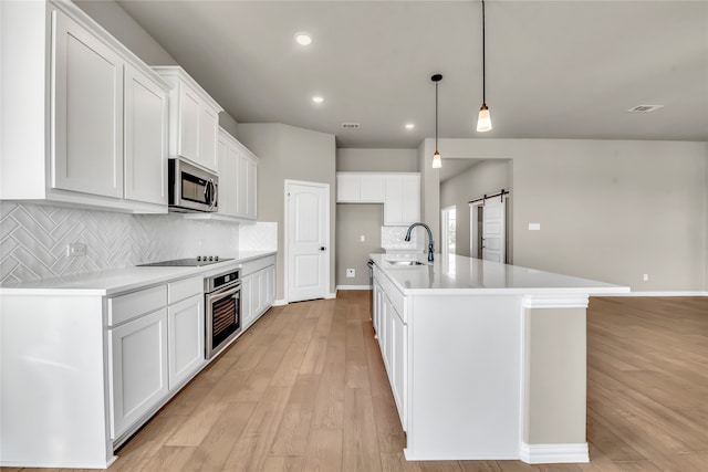 kitchen featuring a barn door, white cabinetry, stainless steel appliances, and a kitchen island with sink