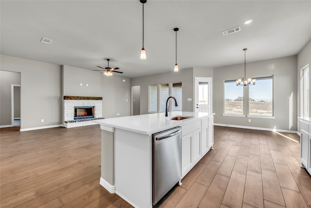 kitchen featuring light wood-type flooring, sink, a center island with sink, dishwasher, and hanging light fixtures