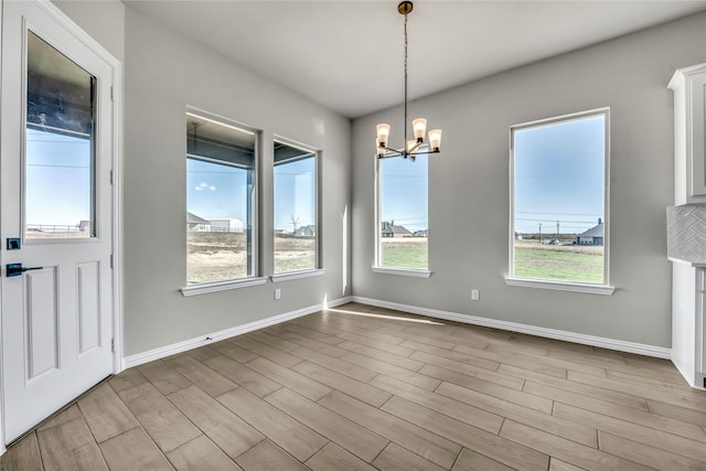 unfurnished dining area with light wood-type flooring, a wealth of natural light, and a chandelier