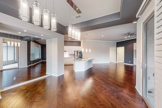 interior space featuring white cabinets, an island with sink, stainless steel fridge, decorative light fixtures, and dark wood-type flooring