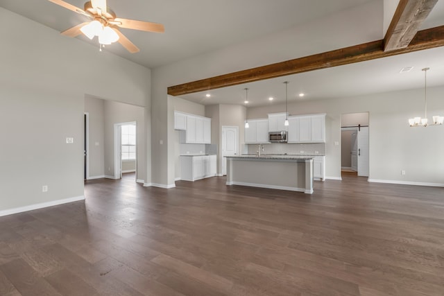 unfurnished living room featuring beamed ceiling, sink, dark hardwood / wood-style flooring, ceiling fan with notable chandelier, and a barn door