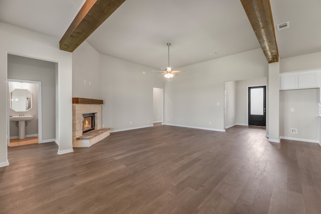 unfurnished living room featuring a fireplace, dark hardwood / wood-style floors, beamed ceiling, and ceiling fan