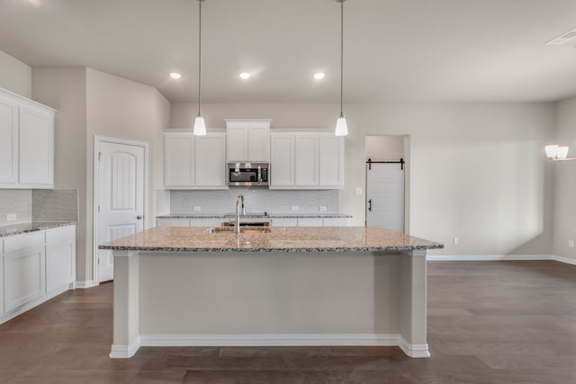 kitchen with dark wood-type flooring, light stone counters, a barn door, and white cabinetry