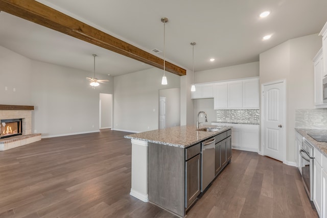 kitchen featuring a kitchen island with sink, stainless steel appliances, dark wood-type flooring, white cabinetry, and beam ceiling