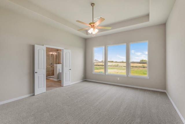 unfurnished bedroom with ceiling fan, light colored carpet, a tray ceiling, and ensuite bathroom