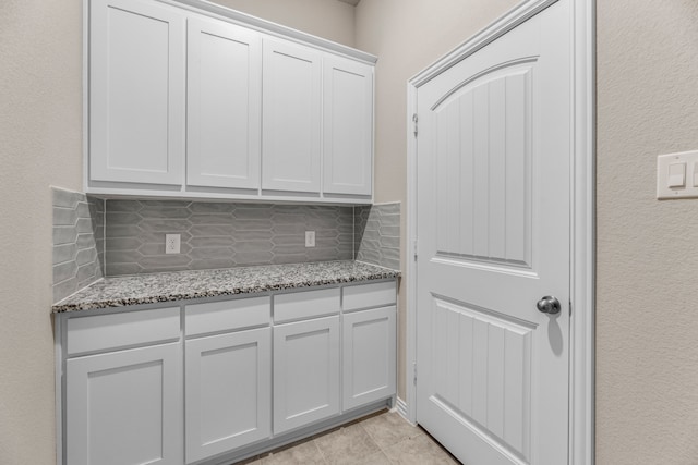 kitchen featuring light tile patterned flooring, light stone counters, white cabinetry, and backsplash