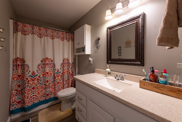 bathroom featuring wood-type flooring, walk in shower, vanity, and toilet