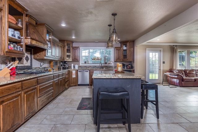 kitchen with an island with sink, a kitchen bar, custom exhaust hood, appliances with stainless steel finishes, and light stone countertops