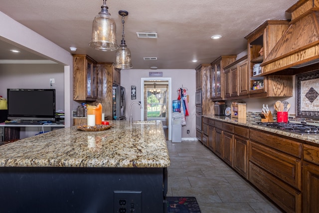 kitchen with light stone counters, a center island with sink, hanging light fixtures, and sink