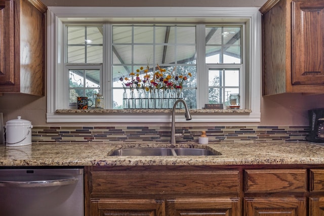 kitchen featuring stainless steel dishwasher, sink, light stone counters, and tasteful backsplash