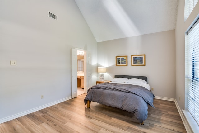 bedroom with ensuite bath, light hardwood / wood-style floors, and high vaulted ceiling