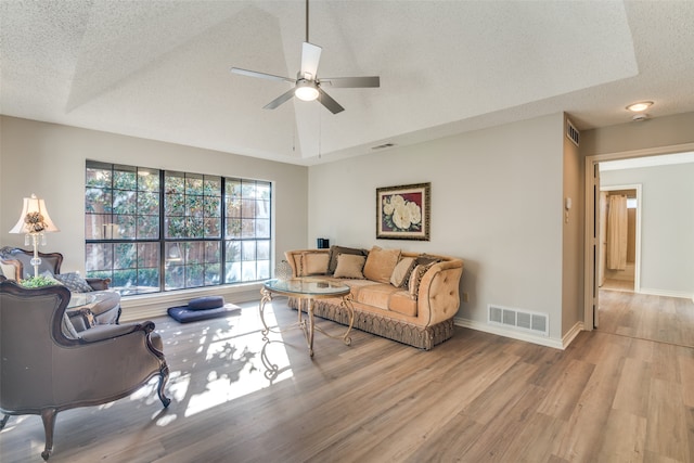 living room featuring a textured ceiling, a tray ceiling, light wood-type flooring, and ceiling fan