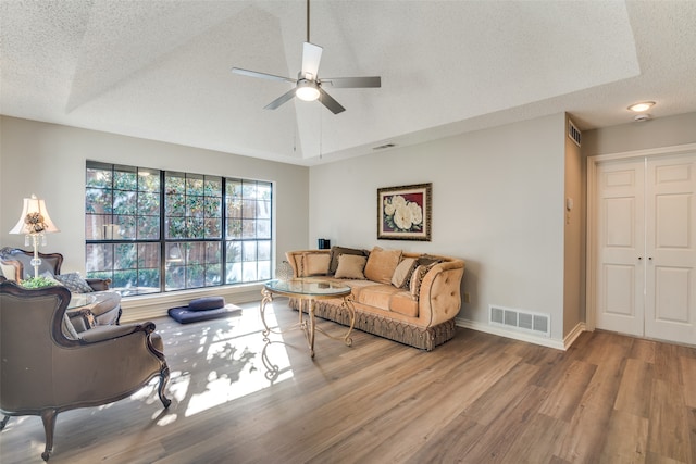 living room with a textured ceiling, a tray ceiling, hardwood / wood-style floors, and ceiling fan