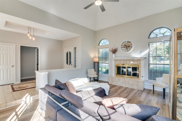 living room with ceiling fan, light hardwood / wood-style flooring, a fireplace, and a high ceiling