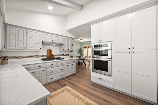 kitchen featuring appliances with stainless steel finishes, white cabinets, backsplash, beamed ceiling, and light wood-type flooring