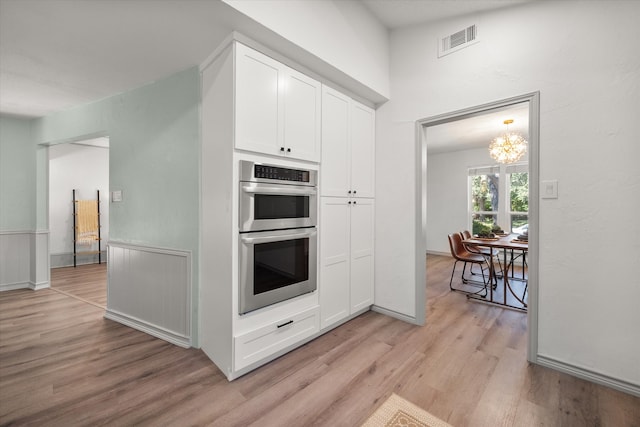 kitchen featuring a notable chandelier, double oven, light hardwood / wood-style flooring, and white cabinets