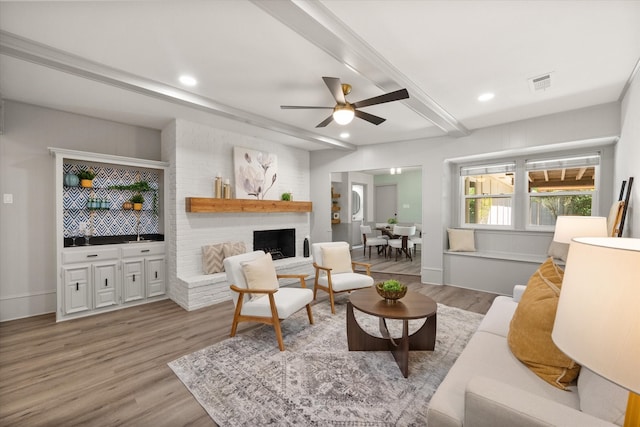 living room featuring ceiling fan, beamed ceiling, a fireplace, and light hardwood / wood-style floors