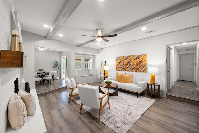 living room with a brick fireplace, ceiling fan, beamed ceiling, and hardwood / wood-style flooring