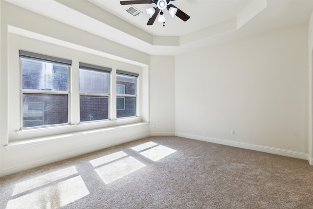 empty room featuring carpet floors, a raised ceiling, and ceiling fan