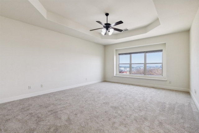 spare room featuring ceiling fan, light colored carpet, and a raised ceiling