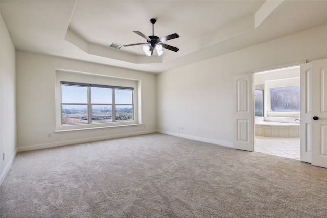 carpeted spare room featuring ceiling fan and a raised ceiling