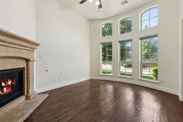 unfurnished living room with ceiling fan, a towering ceiling, dark hardwood / wood-style flooring, and a tile fireplace