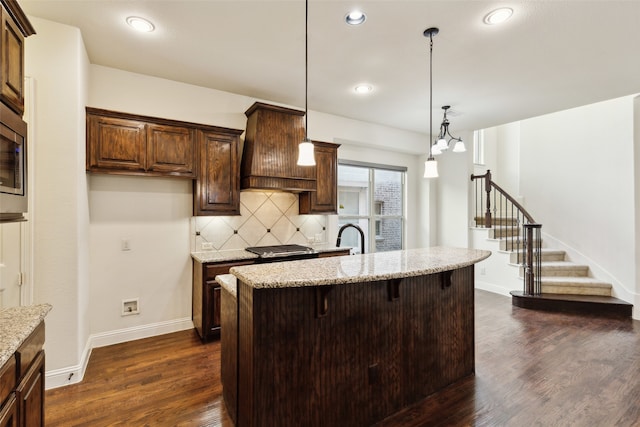 kitchen featuring pendant lighting, light stone counters, a kitchen bar, and dark hardwood / wood-style flooring